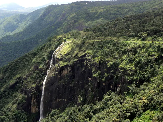 In this image there are mountains, trees and a waterfall.